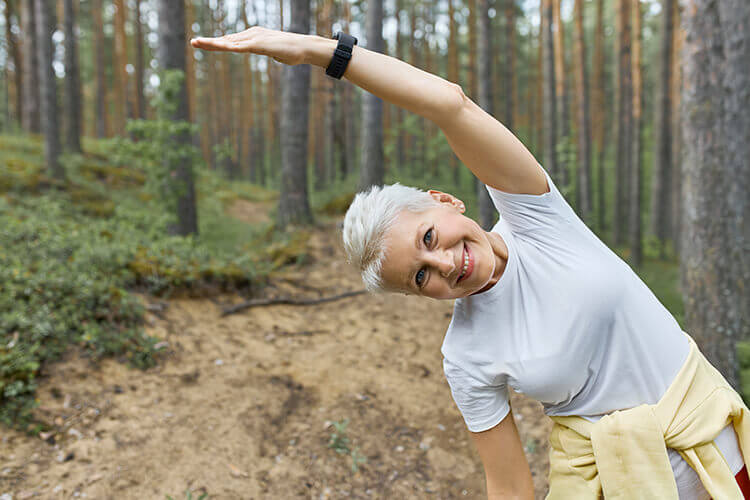 energetic active middle aged female warming body before running posing against pine trees 1